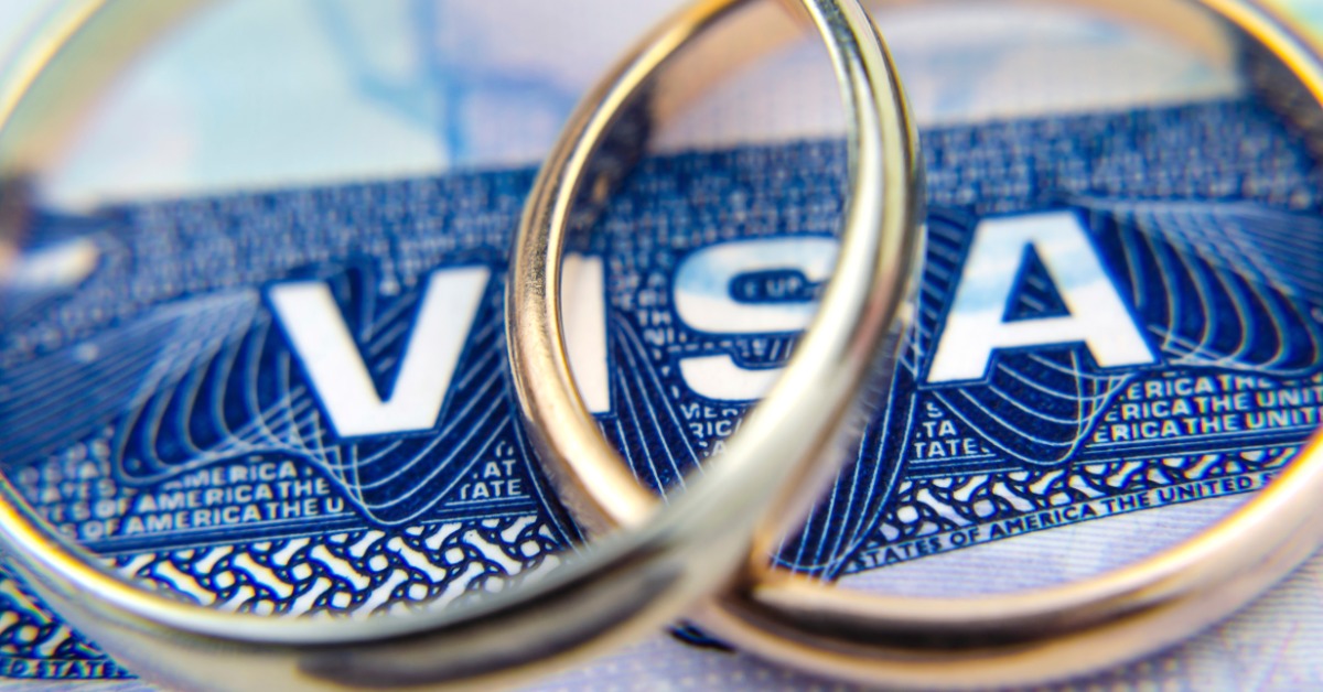 A close-up of a U.S. entry visa in a passport with two wedding rings resting nearby on the visa page.