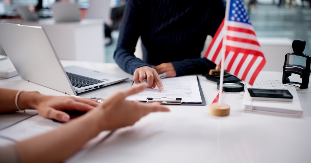 a woman reviewing visa application documents while sitting at a desk with a passport and laptop nearby.