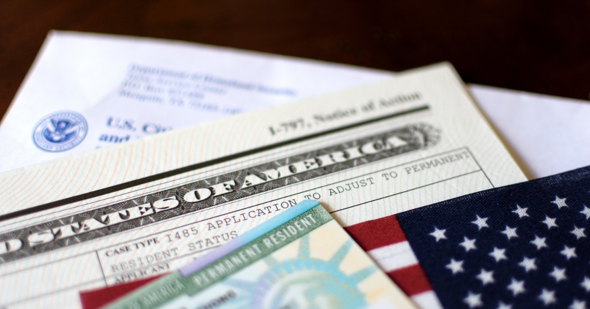 a permanent resident card placed beside a passport and small United States flag on a white surface.