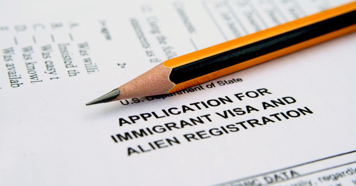 A yellow and black pencil lying across an application for immigrant visa and alien registration form.
