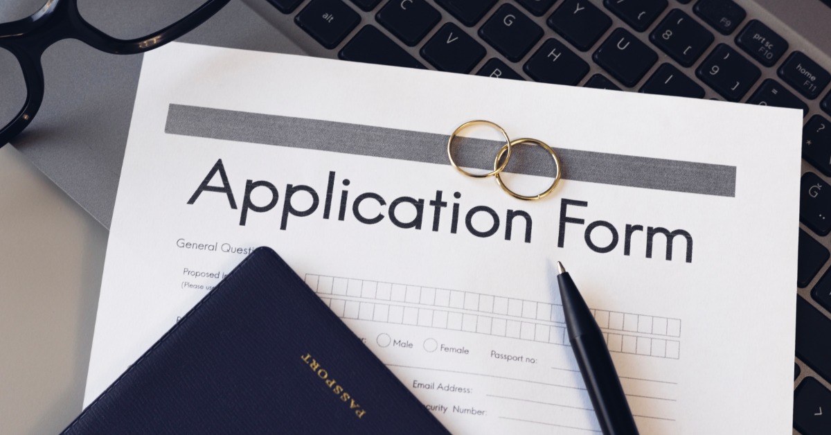 a passport and a black pen resting on a printed application form with two rings and a laptop keyboard nearby.
