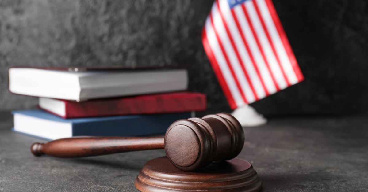 A wooden gavel resting on a round block with stacked books and a small United States flag on a dark surface.